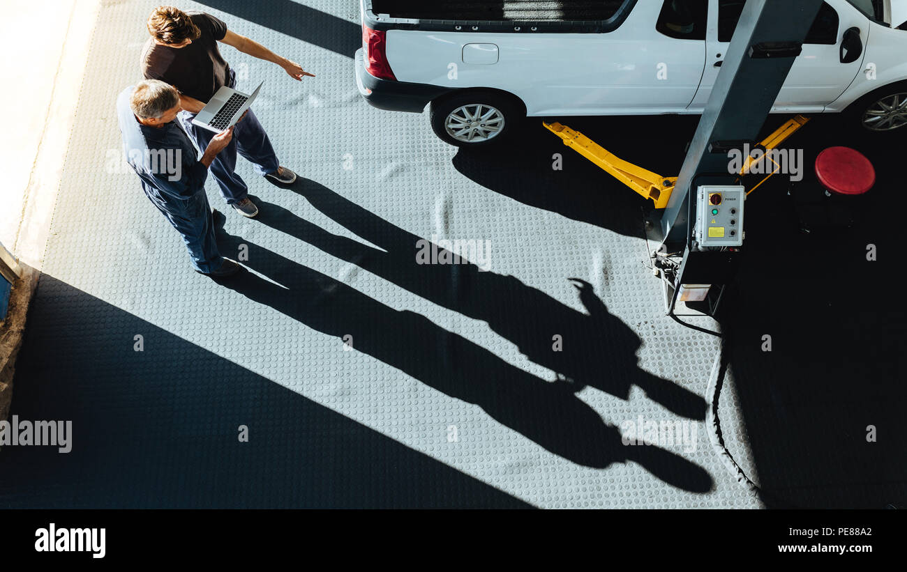 Vista superiore della macchina professionale meccanica a lavorare nel negozio di riparazioni auto con il computer portatile. Meccanica tramite computer portatile per diagnosticare l'auto. Foto Stock