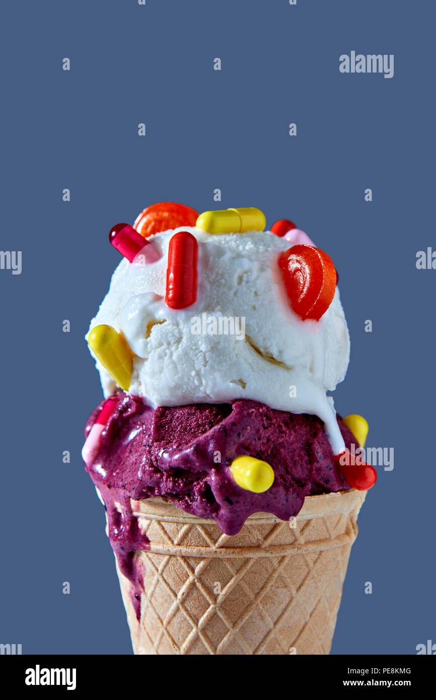 Il freddo deliziosi gelati in un cono di cialda con il rosso e il giallo pillole e un lecca-lecca contro uno sfondo blu. Close-up. Foto Stock