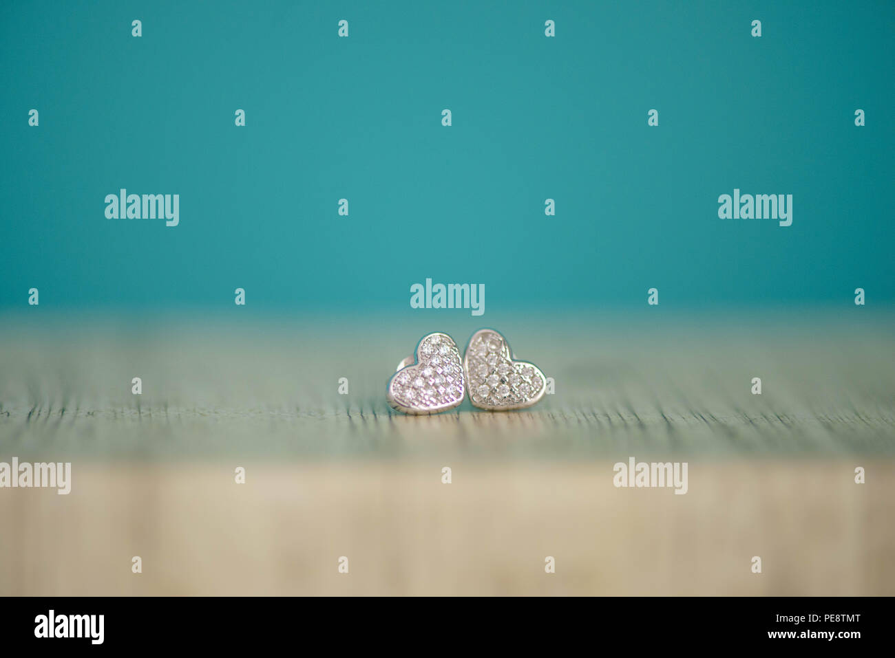 A forma di cuore ad argento coppia di orecchini con autentico o similpelle di diamanti, visualizzata su un tavolo in legno con il fuoco selettivo e blu sullo sfondo colorato Foto Stock