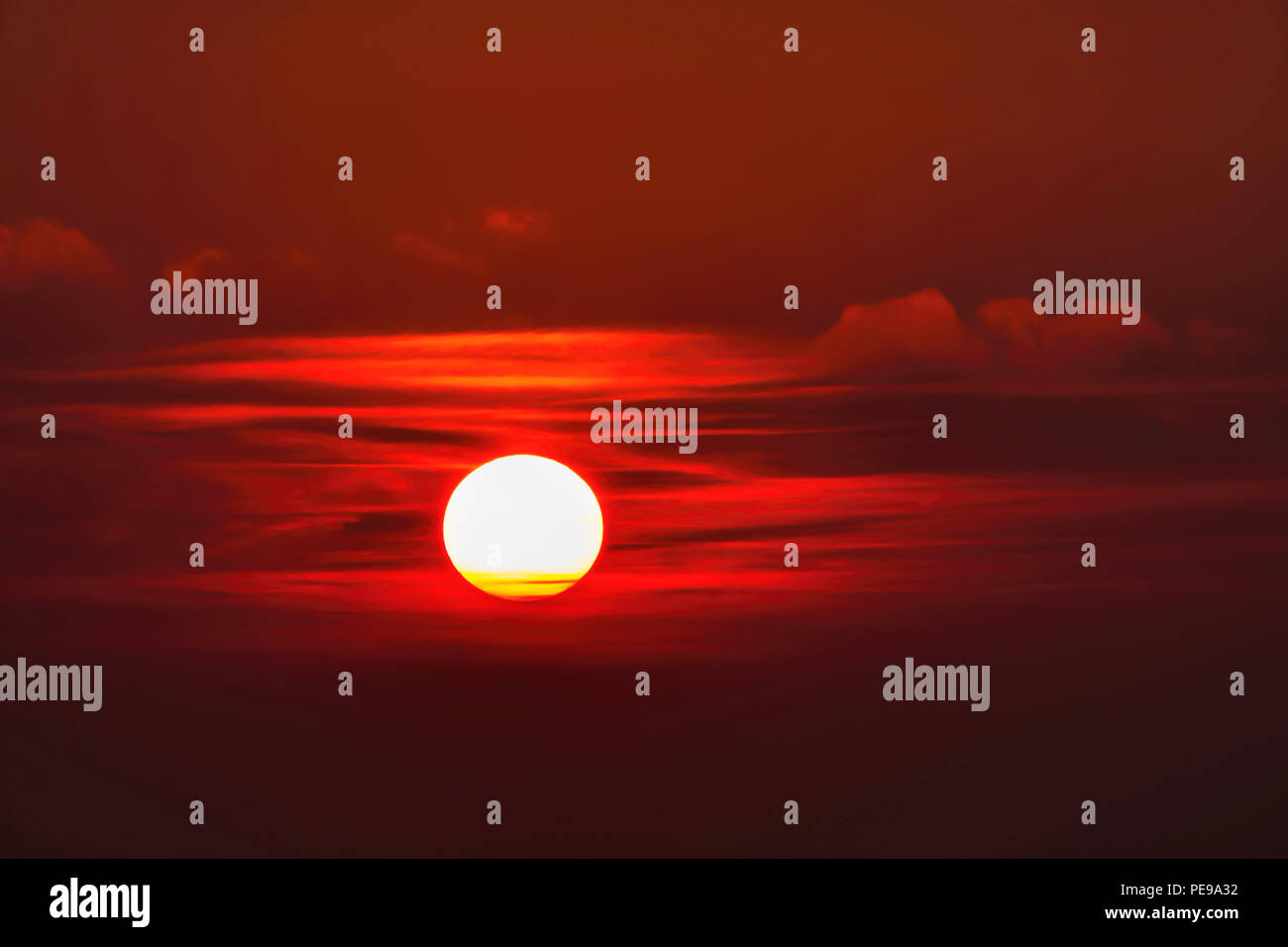 Il sole verso il tramonto tra le nuvole si diffonde una luce rossa Foto Stock