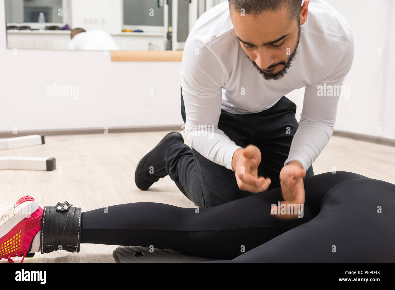Maschio adulto trainer con camicia bianca womans massaggiante coscia in palestra con pavimento in legno e pareti di colore bianco Foto Stock