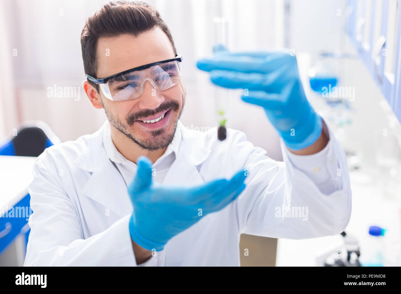 Progresso scientifico. Jolly gay laboratorian maschio indossando un vetro di sicurezza mentre la coltivazione di piante in flaconcino e sorridente Foto Stock