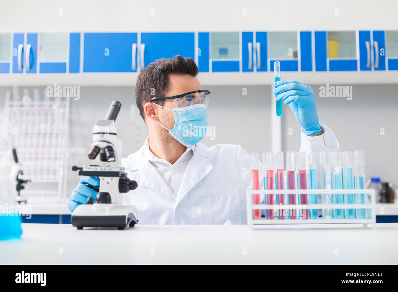 Sfida scientifica. Piacevole bello laboratorian maschile medicazione occhiali di sicurezza mentre elevando la fiala e guardando a esso Foto Stock