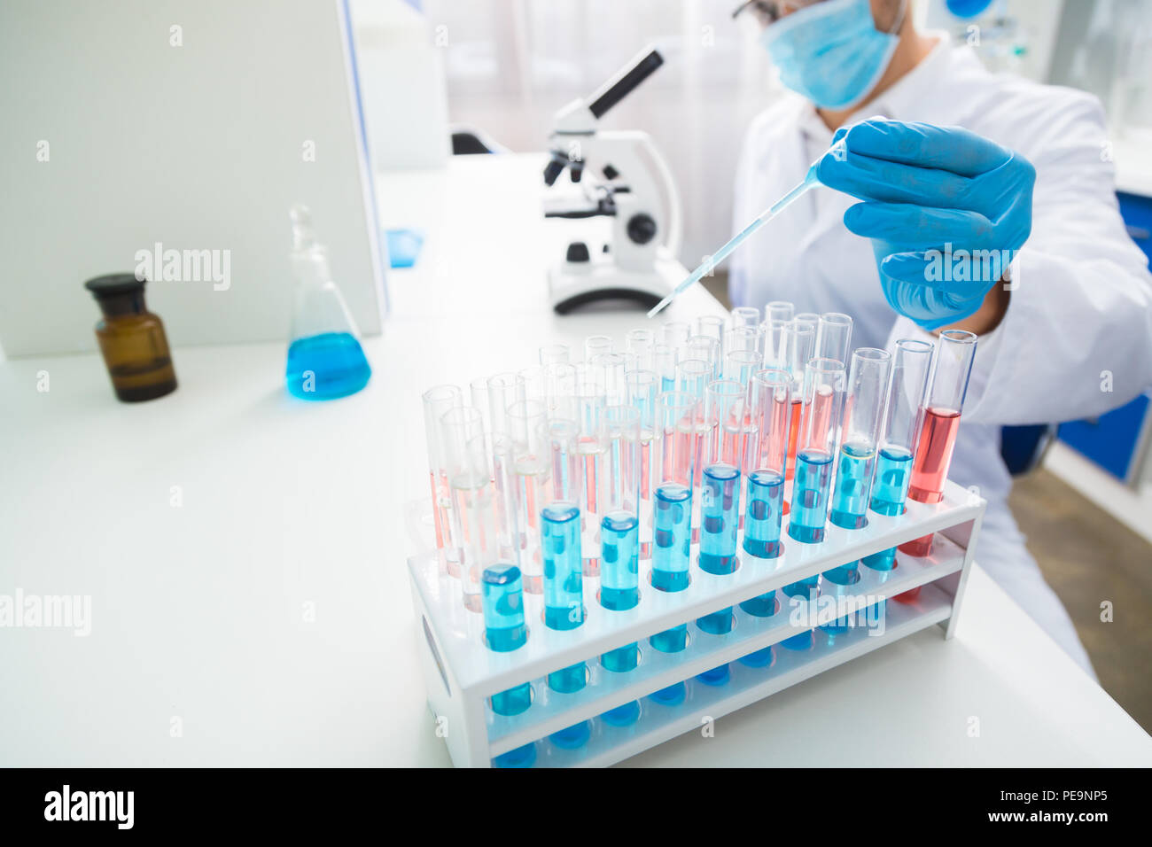 Proporzione precisa. Forte mano maschile medicazione guanti tenendo la pipetta e versando il liquido Foto Stock