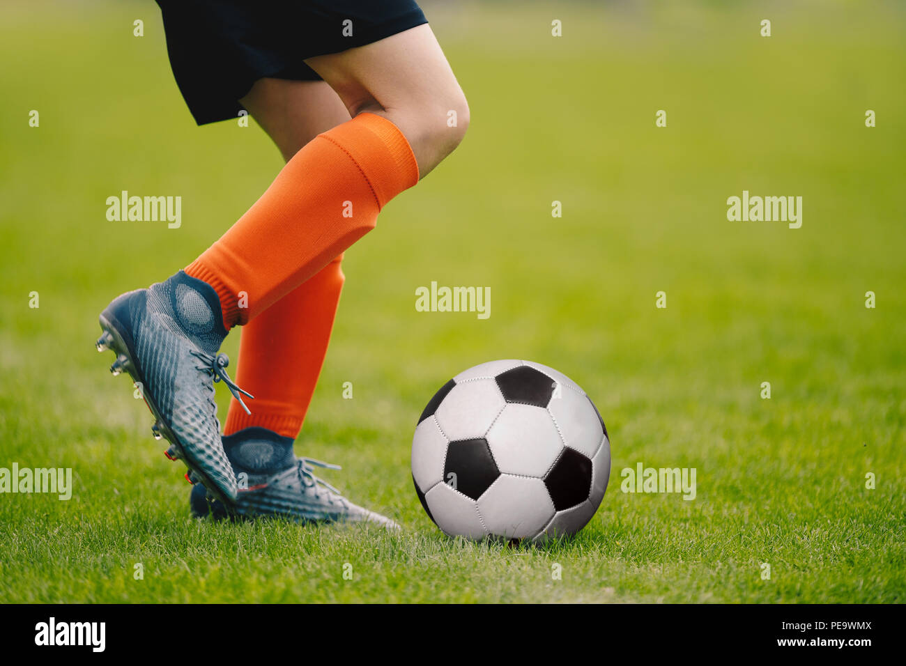 Un giovane uomo di calciare un calcio all'esterno. Giovane calciatore la  formazione su un campo in erba. Ragazzo in un abbigliamento sportivo.  Giocatore di calcio indossare calze arancione e Foto stock -