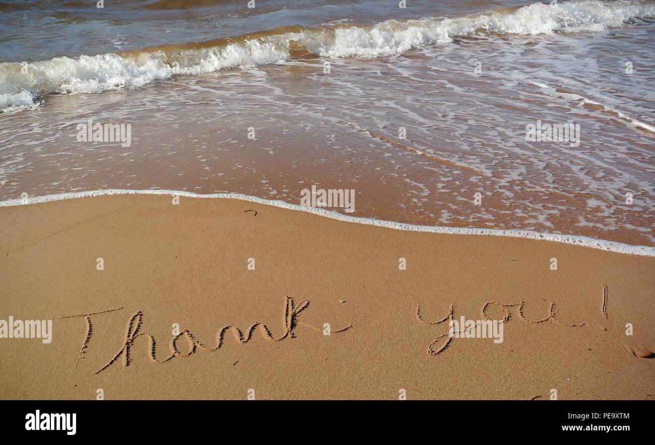 Un bellissimo messaggio di riconoscenza "grazie" scritta a mano in stile corsivo sulla sabbia rossa su una spiaggia con un'onda in arrivo, Prince Edward Island. Foto Stock