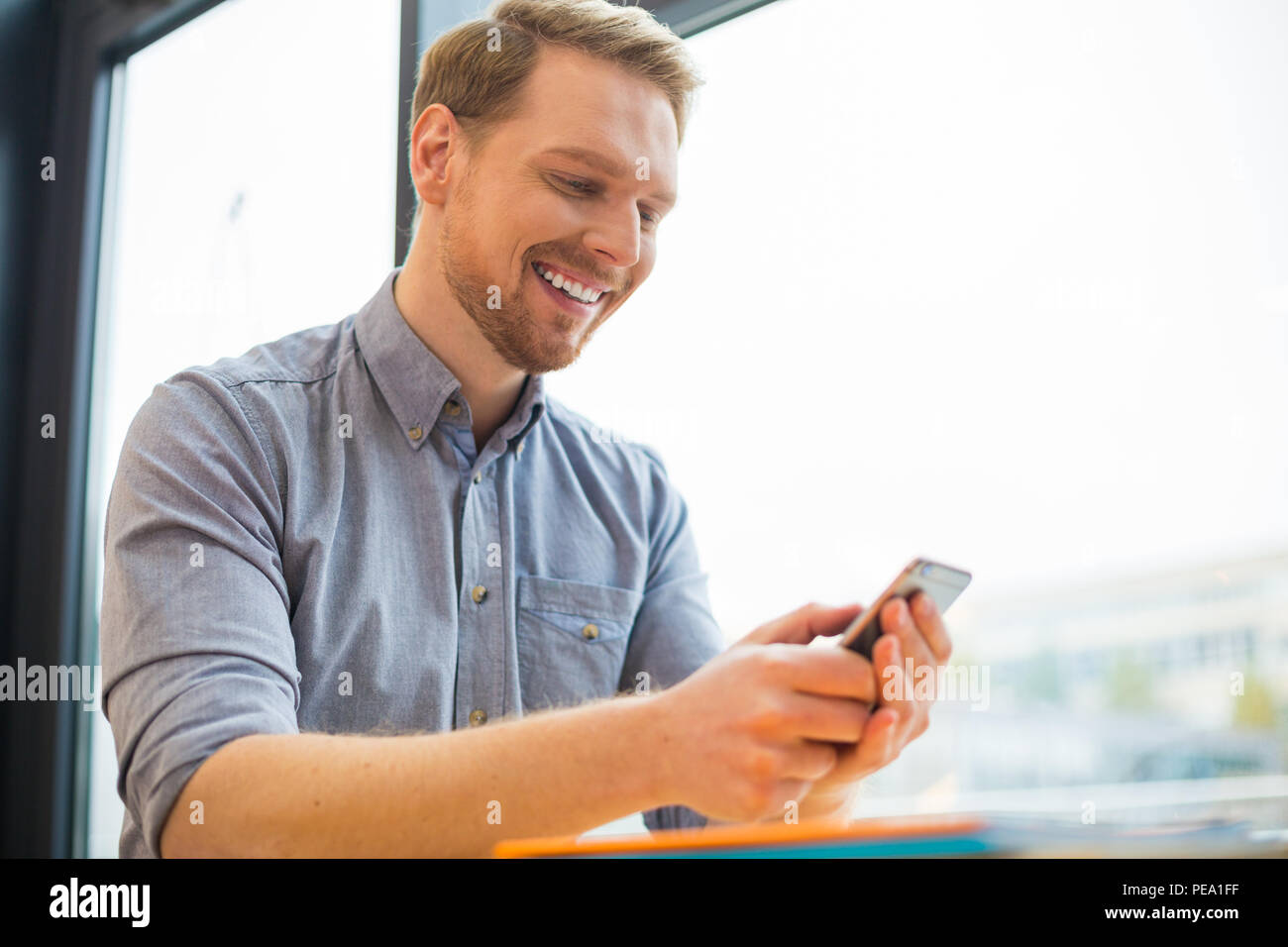 Moderno dispositivo tecnologico. Allegro felice lieto uomo guardando lo schermo dello smartphone e sorridente quando si utilizza questo dispositivo Foto Stock