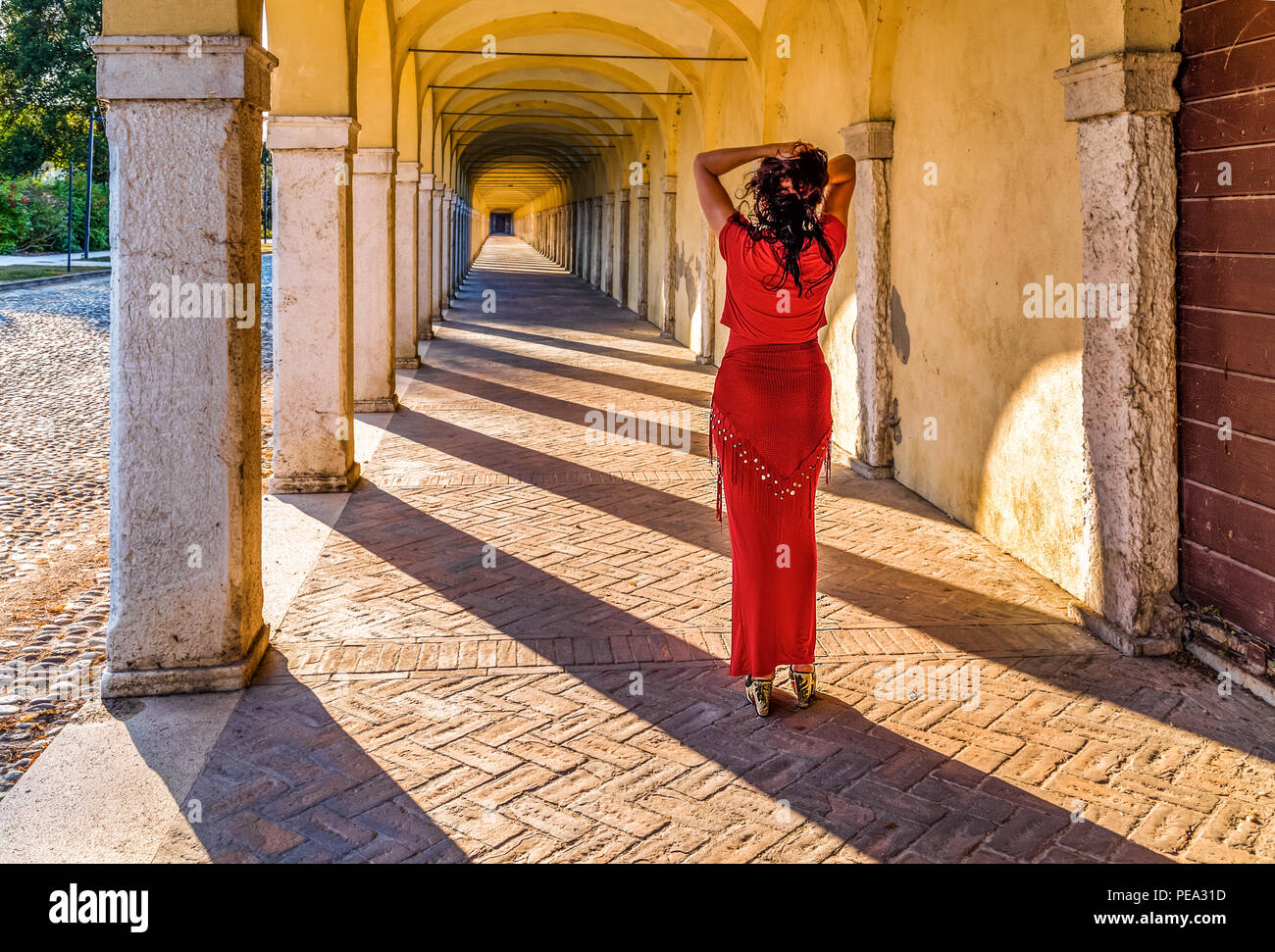 Donna con un corpo sinuoso lei tiene i suoi capelli davanti un lungo porticato guardando al punto di fuga Foto Stock