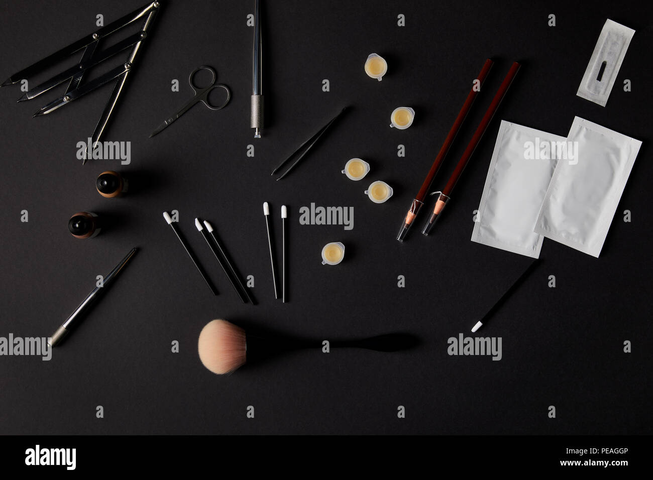Vista dall'alto di spazzole, matite, cosmetici e strumenti per trucco permanente su nero Foto Stock