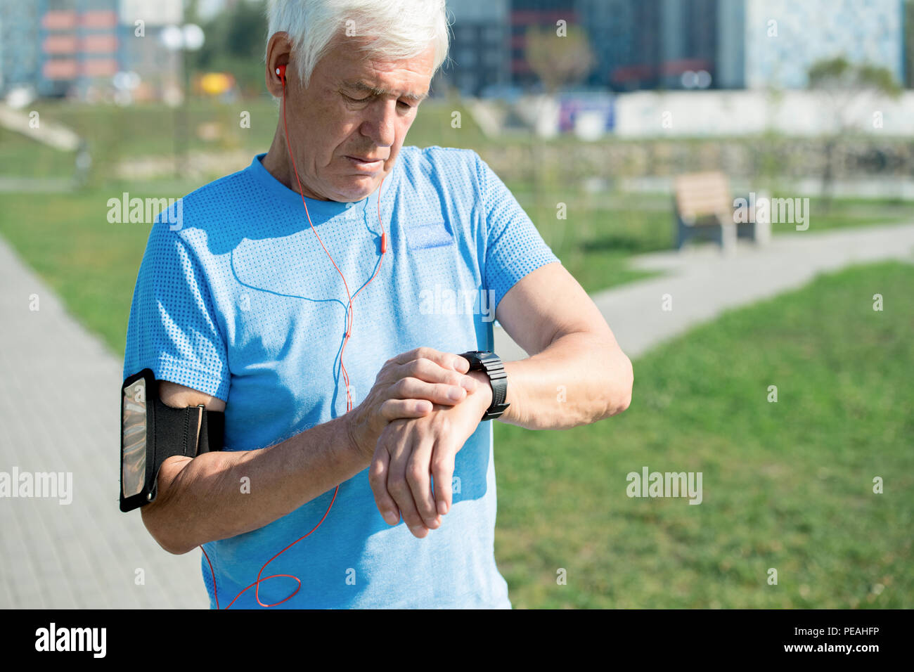 Vita ritratto di moderno uomo senior impostazione smart guardare e ascoltare musica mentre si fa jogging mattutino nel parco, spazio di copia Foto Stock
