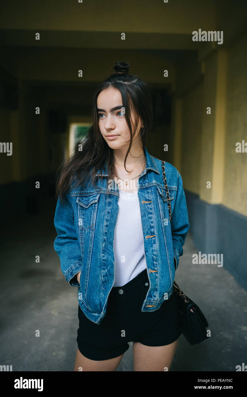 Giovani donne che indossano pantaloncini e tenere le mani nelle tasche di  denim blu con giacca con espressione indifferente sul suo viso che guarda  lontano. Teen girl in piedi Foto stock -