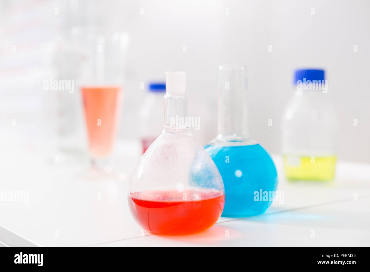 Esperimento di chimica. Vetro cristallo lampadine in piedi su superfici di bianco e riempito con reagente Foto Stock