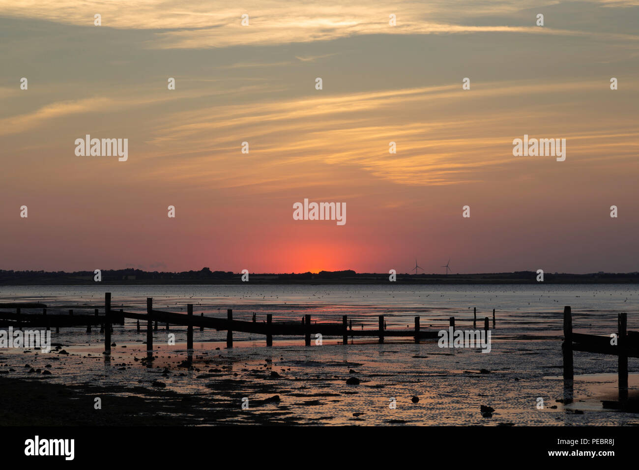 Il sole solo scomparendo oltre l'orizzonte preso dalla spiaggia Seasalter, Kent, Regno Unito guardando verso l'Isle of Sheppey. Il vecchio le difese del mare sono visibili. Foto Stock
