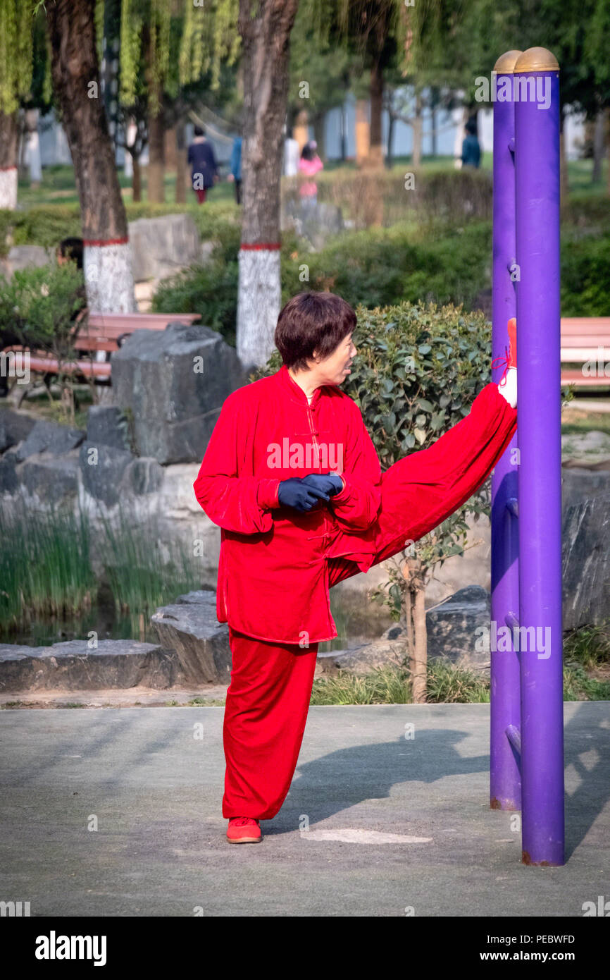 Una mezza età donna cinese il suo allungamento della gamba in un parco giochi, Xi'an, Cina Foto Stock