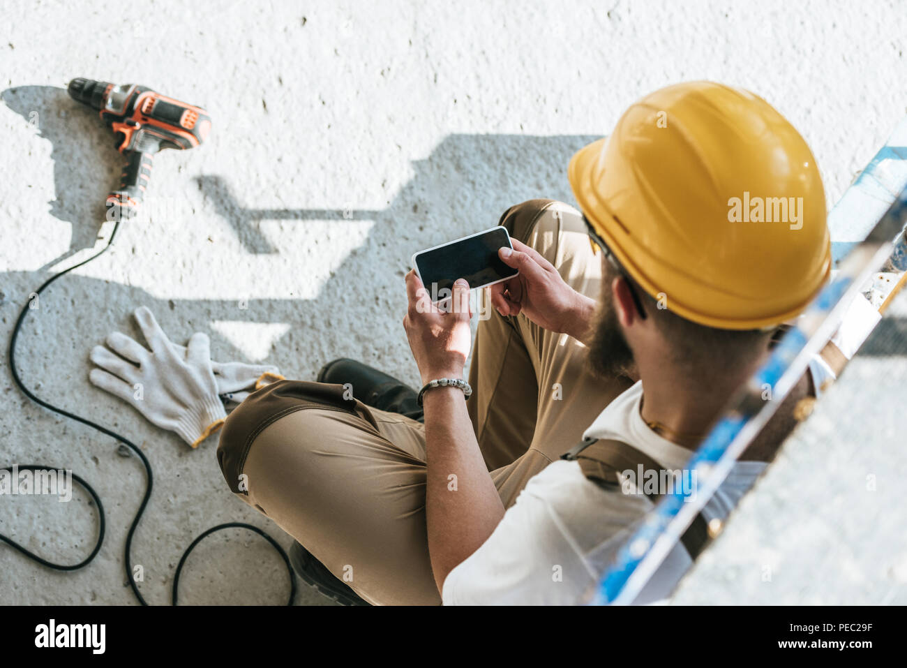 Vista aerea del costruttore nel casco di protezione utilizza lo smartphone con schermo vuoto al sito in costruzione Foto Stock