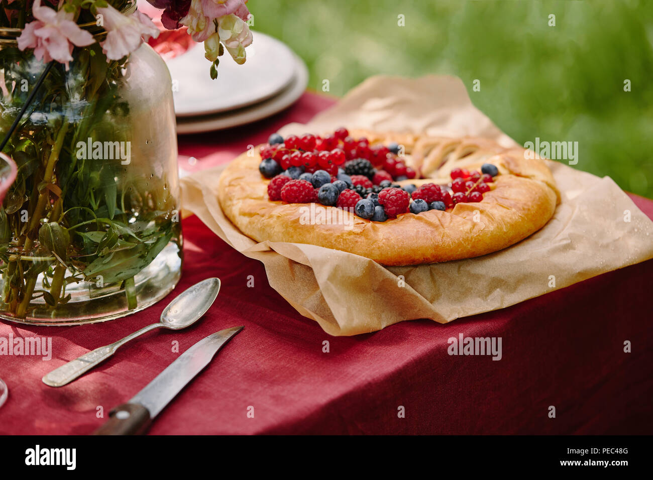 Gustosa torta con lamponi, ribes e mirtilli sul tavolo in giardino Foto Stock Gustosa torta con lamponi, ribes e mirtilli sul tavolo in giardino Foto Stock