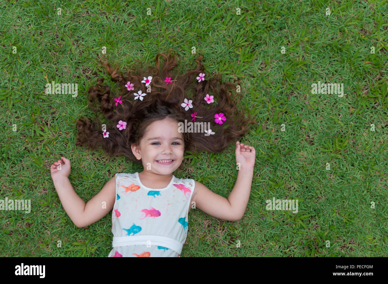 Bella e felice ragazza a giocare nel parco con prato meraviglioso e fiori, sorriso con abito leggero e capelli ondulati, bella ragazza brasiliana con brow Foto Stock