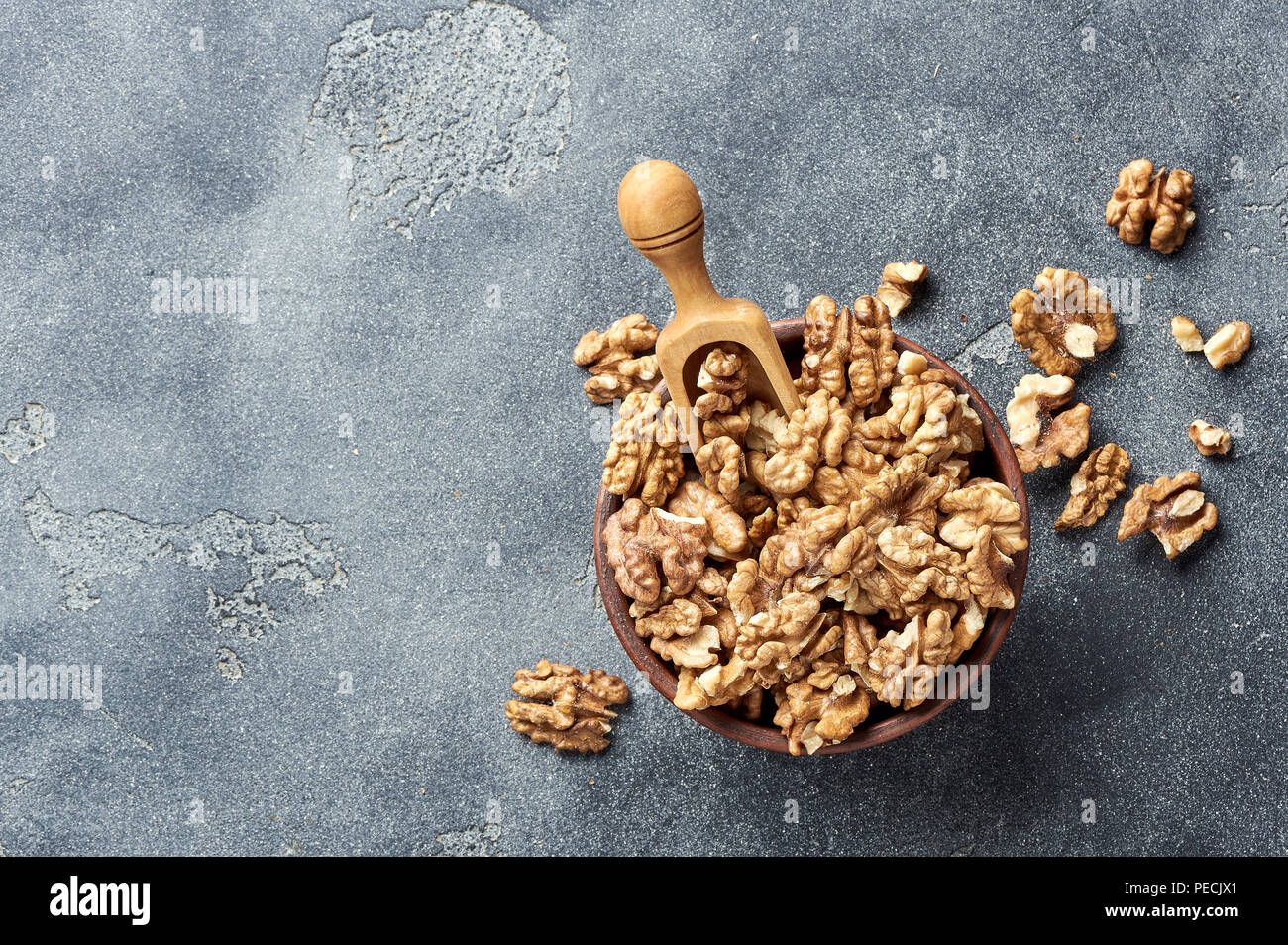 Gherigli di noce con il cucchiaio di legno su sfondo grigio con copia spazio. I dadi nel recipiente di argilla. Vista dall'alto. Foto Stock