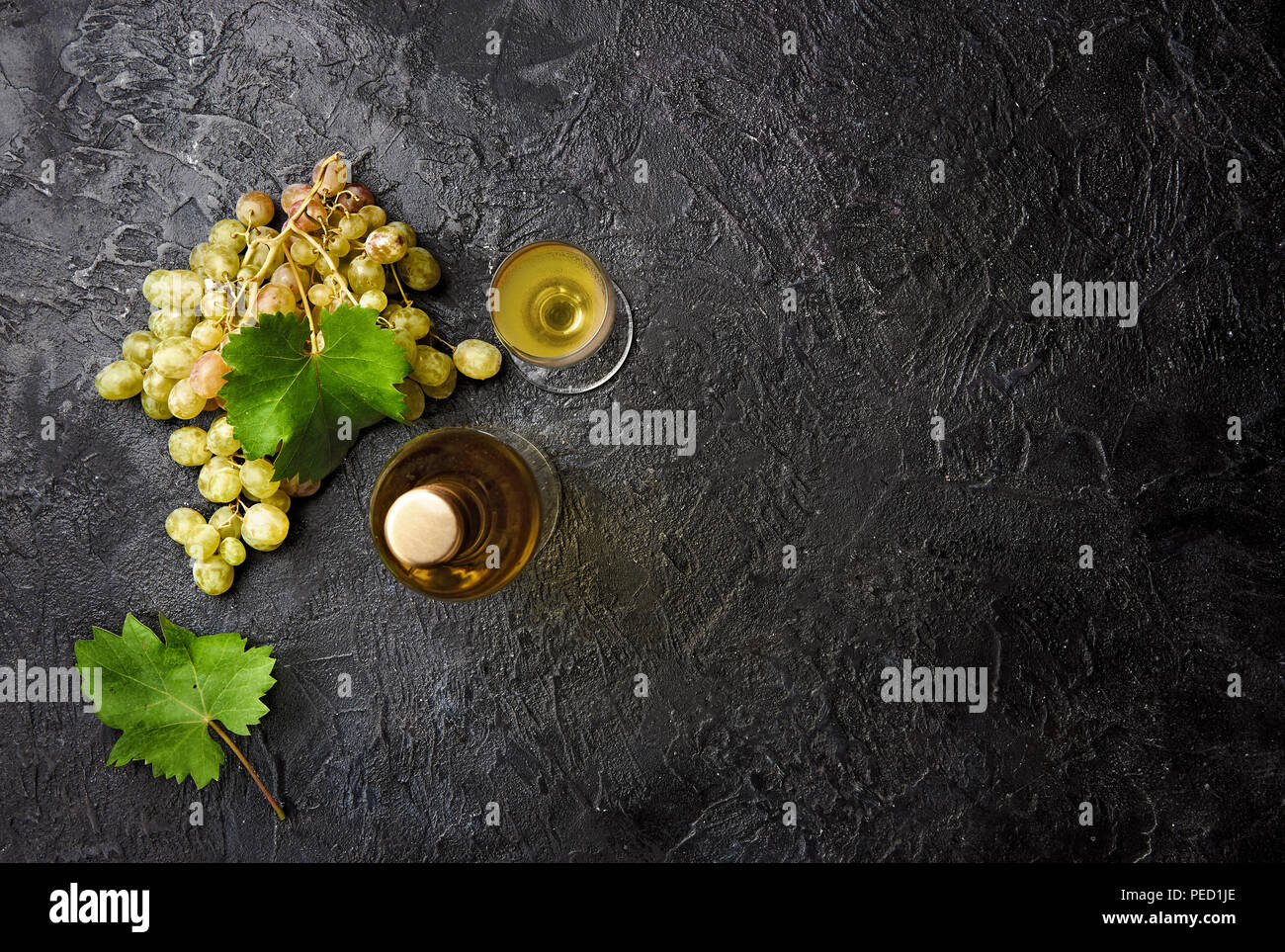 Bottiglia di vino bianco con uve e foglie di uve sul calcestruzzo scuro dello sfondo. Foto Stock