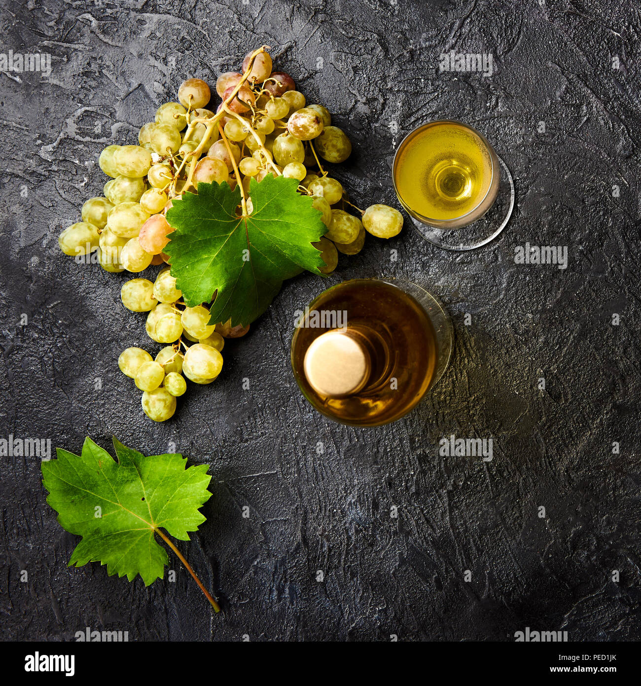 Bottiglia di vino bianco con uve e foglie di uve sul calcestruzzo scuro dello sfondo. Foto Stock