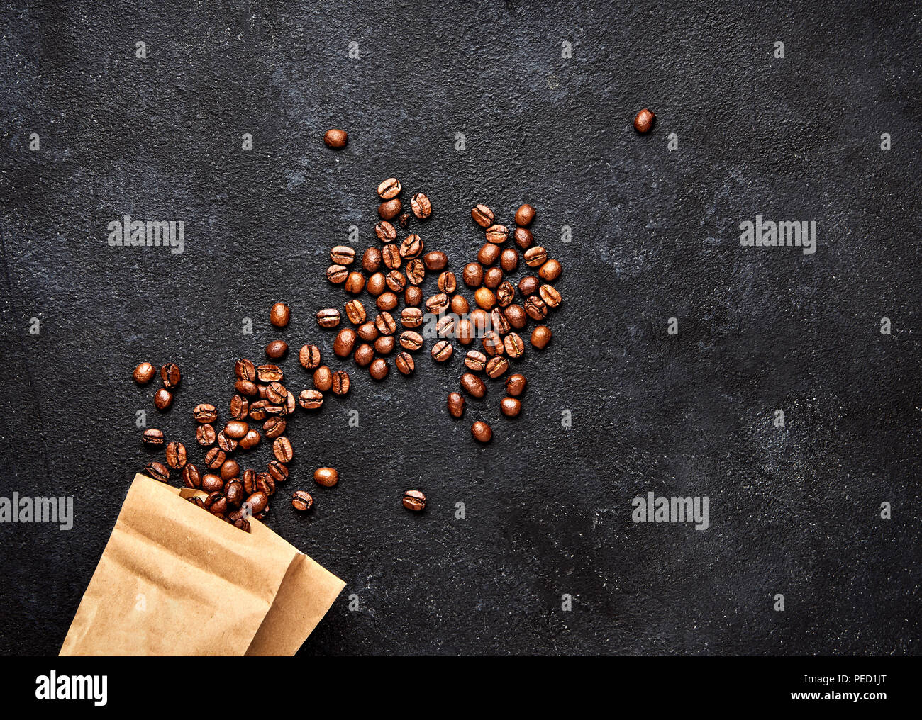 Chicchi di caffè nero su sfondo di calcestruzzo con pacchetto di carta. Vista superiore Foto Stock