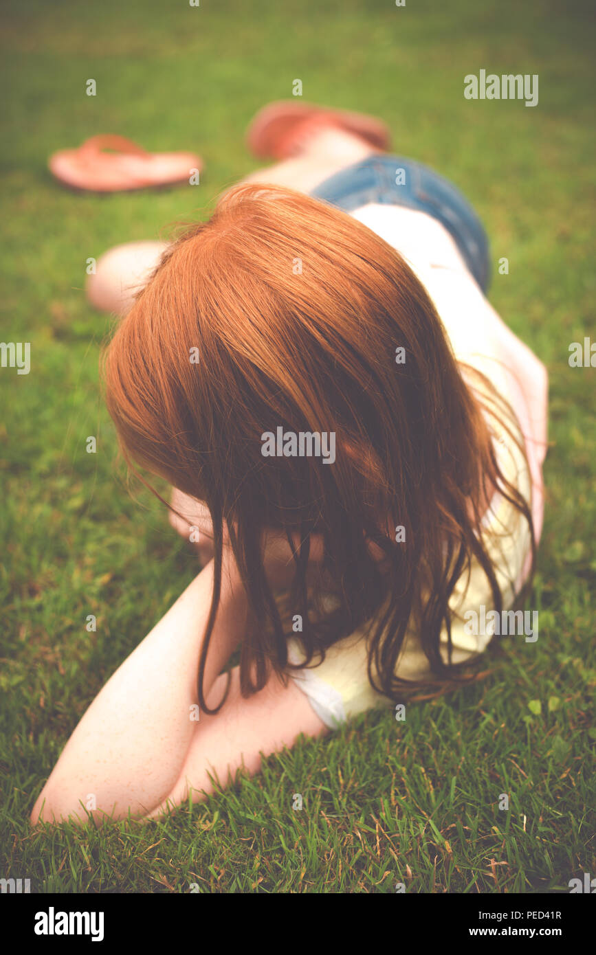 Una giovane ragazza scozzese con i capelli rossi si trova sull'erba in un giardino durante le vacanze estive Foto Stock