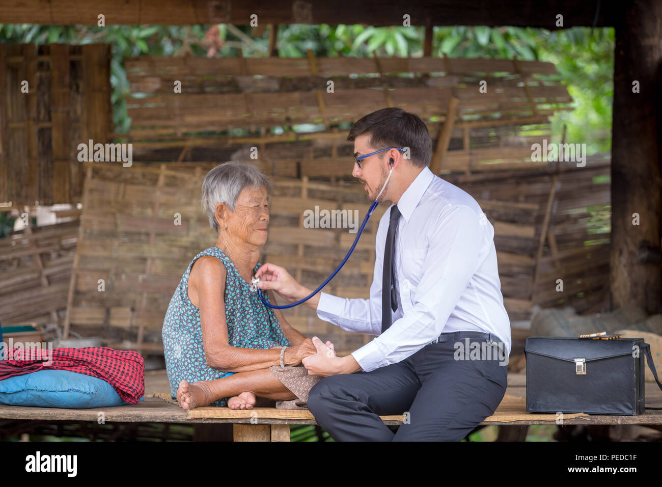 Donna anziana riceve una visita dal medico al paziente a casa o all'aperto. Un medico o medici volontari per visitare gli anziani nelle zone rurali in Asia. Foto Stock
