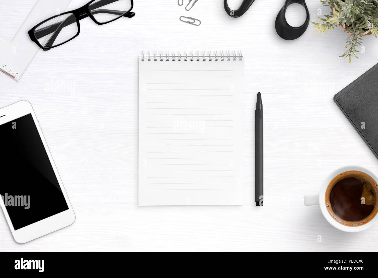 Notebook vuota sulla scrivania in ufficio circondato con la penna, bicchieri, tazza di caffè, telefono cellulare. Appartamento laico, vista dall'alto. Foto Stock