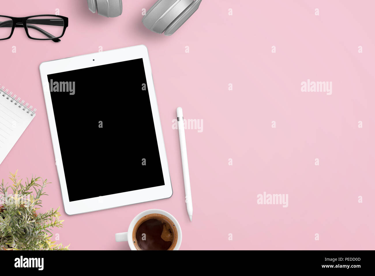 Tablet mockup in rosa scrivania circondata con le cuffie, bicchieri, notepad, impianti, una tazza di caffè e penna. Spazio libero accanto per il testo. Lay piatto compo Foto Stock