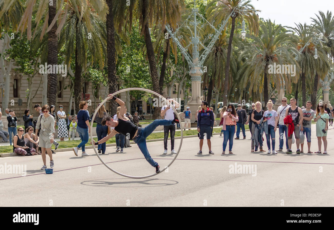 I turisti alla ricerca di attori di strada facendo mosse acrobatiche nel grande anello di metallo, chiamato Cyr ruota o ruota mono a Barcellona Foto Stock