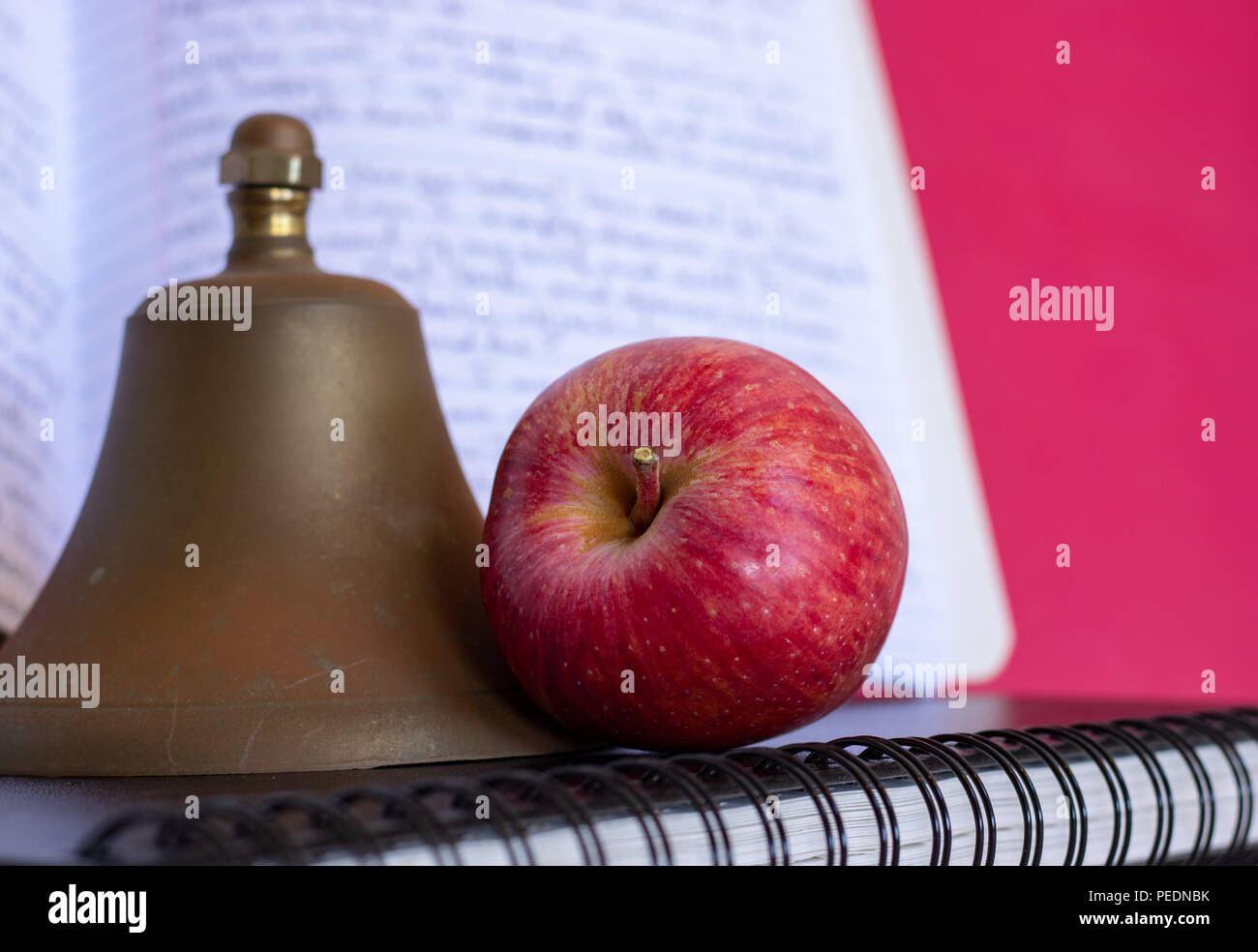 Simboli per l'istruzione, Red delicious homegrown apple, ottone Campanello scuola impilate su nero rilegato a spirale schizzo notebook, cartella rosso e composizione prenota Foto Stock