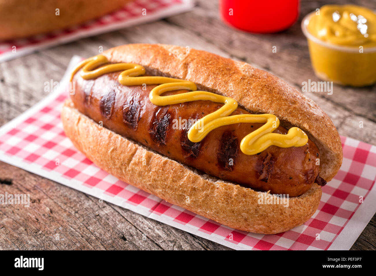 Una deliziosa grigliata di salsiccia affumicata su un rotolo con giallo senape. Foto Stock