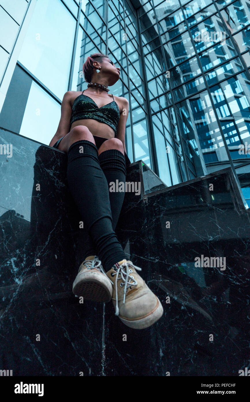Strada ragazza punk in ambiente urbano. Ragazza seduta sulle scale sotto il moderno edificio Foto Stock