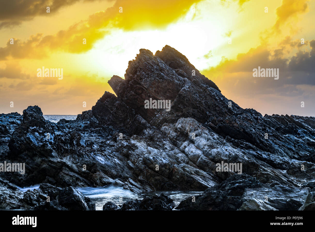 Nuvoloso Tramonto sull'oceano e la spiaggia rocciosa Foto Stock