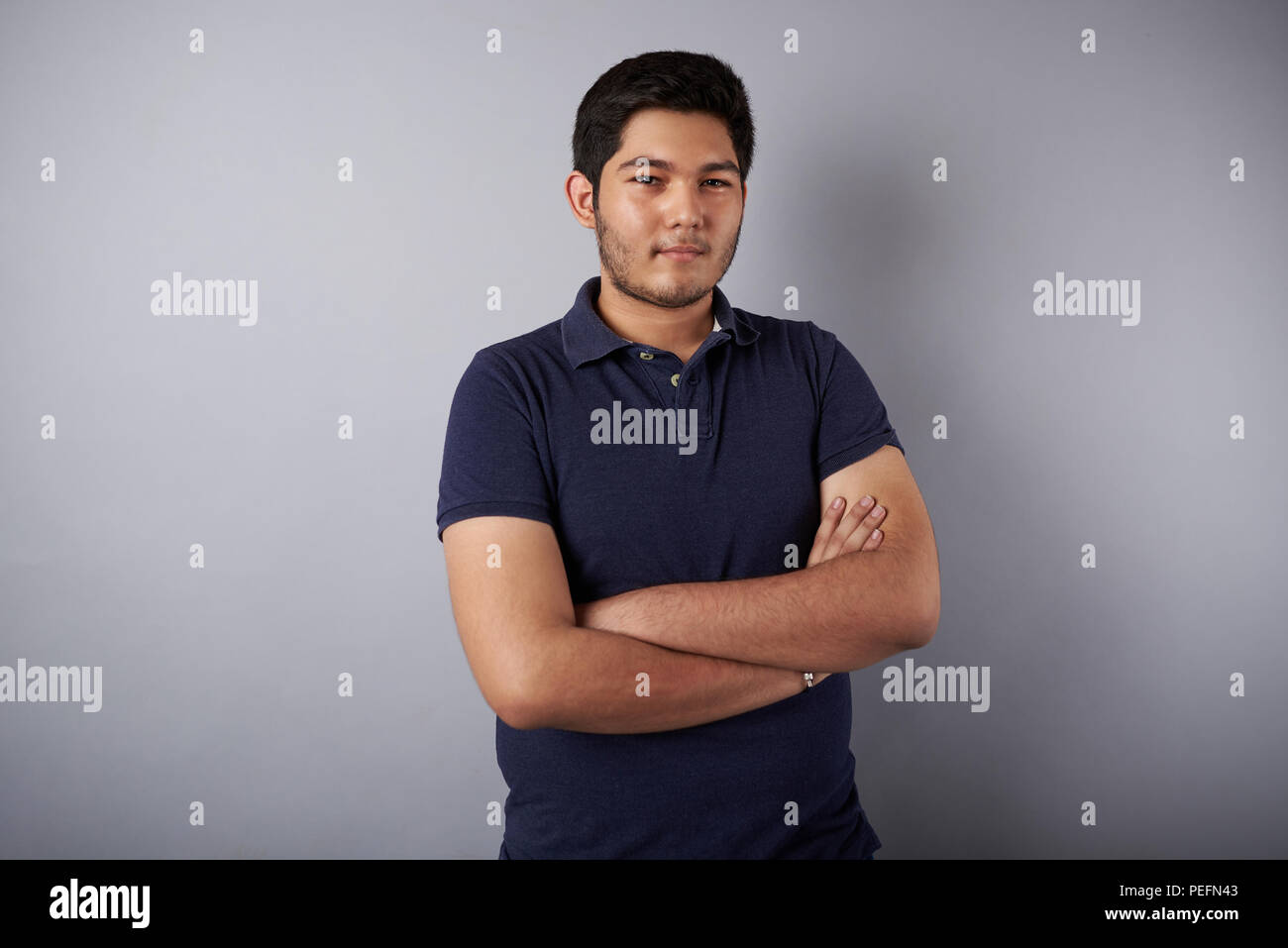 Giovane uomo latino con bracci incrociati su grigio di sfondo per studio Foto Stock
