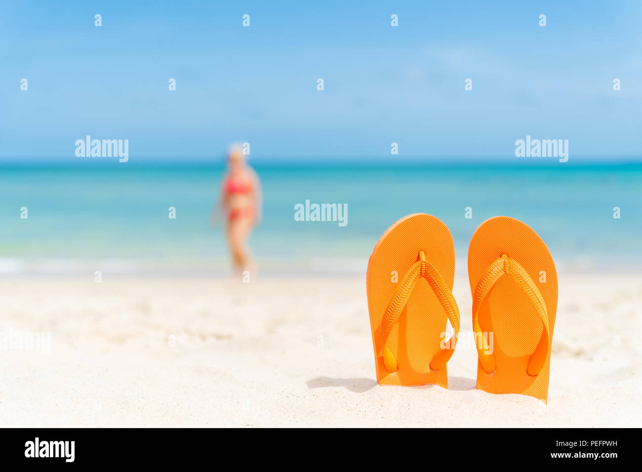 Felice bella giovane donna in bikini rosa con flip flop sulla spiaggia sabbiosa, verde mare e cielo azzurro sfondo per le vacanze estive e il concetto di vacanza. Foto Stock