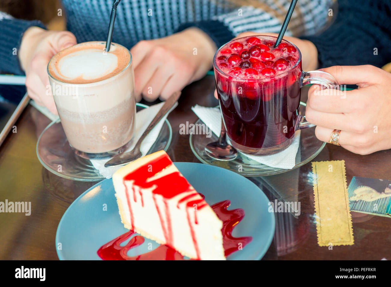 Mani femminili con bevande calde e dessert sul tavolo in un caffè Foto Stock