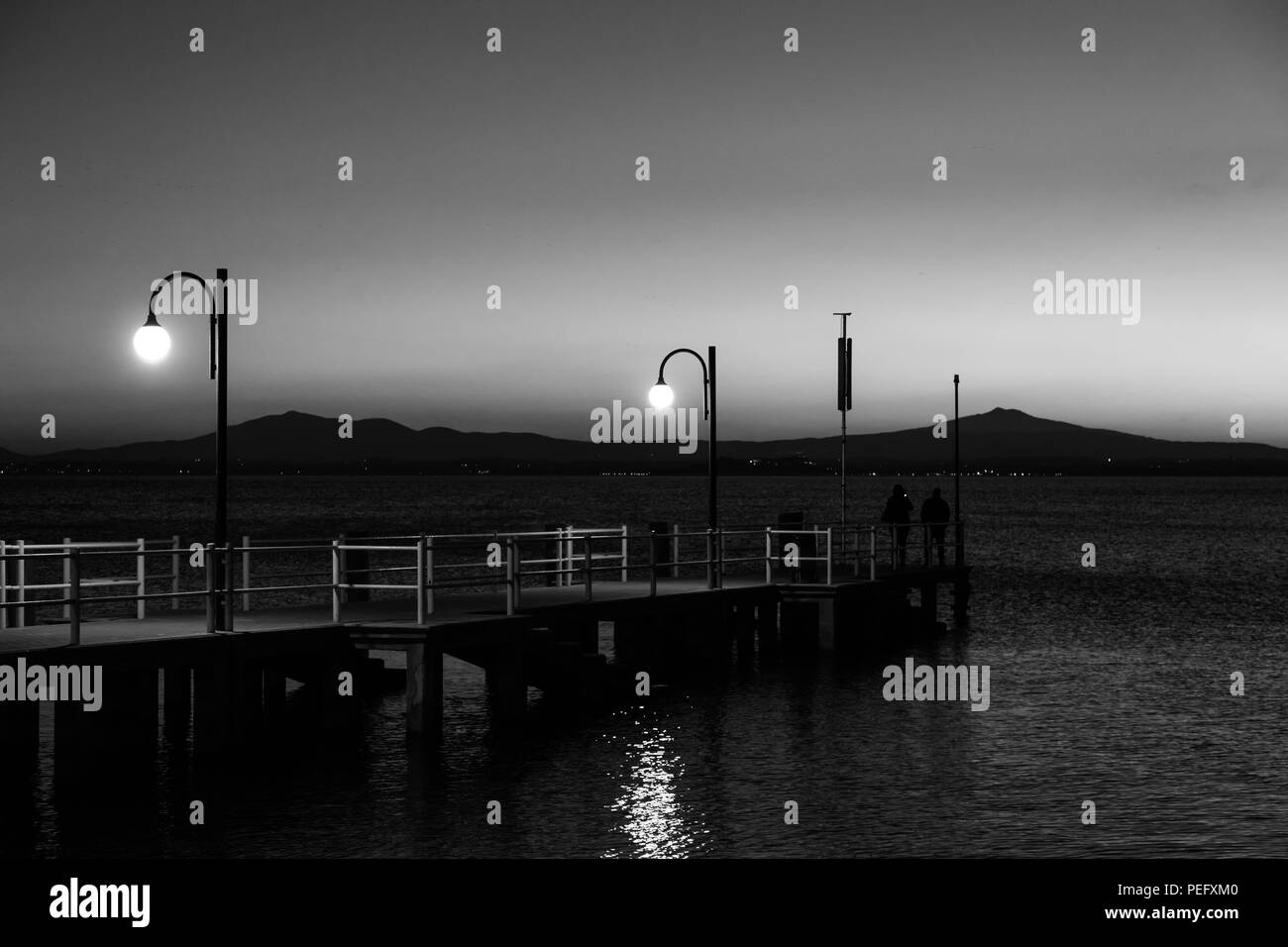 Alcune persone su un molo presso il lago Trasimeno (Umbria, Italia) al tramonto Foto Stock