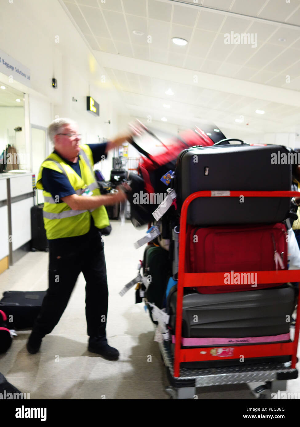 Il bagaglio a mano del gestore di carico bagagli persi utilizzando le strutture presso gli arrivi a Manchester International Airportat l'Aeroporto Internazionale di Manchester Foto Stock