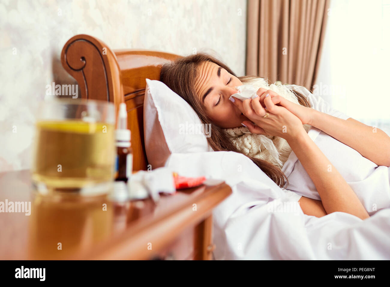Un malato ragazza distesa su un letto tergi il suo naso con una felpa. Foto Stock