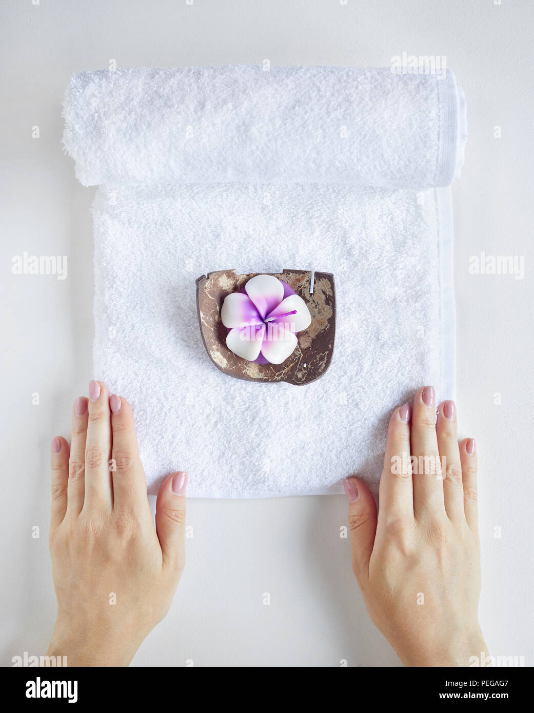 Spa e trattamento. Donna che mantiene asciugamano bianco con candela viola bianco su sfondo semplice Foto Stock