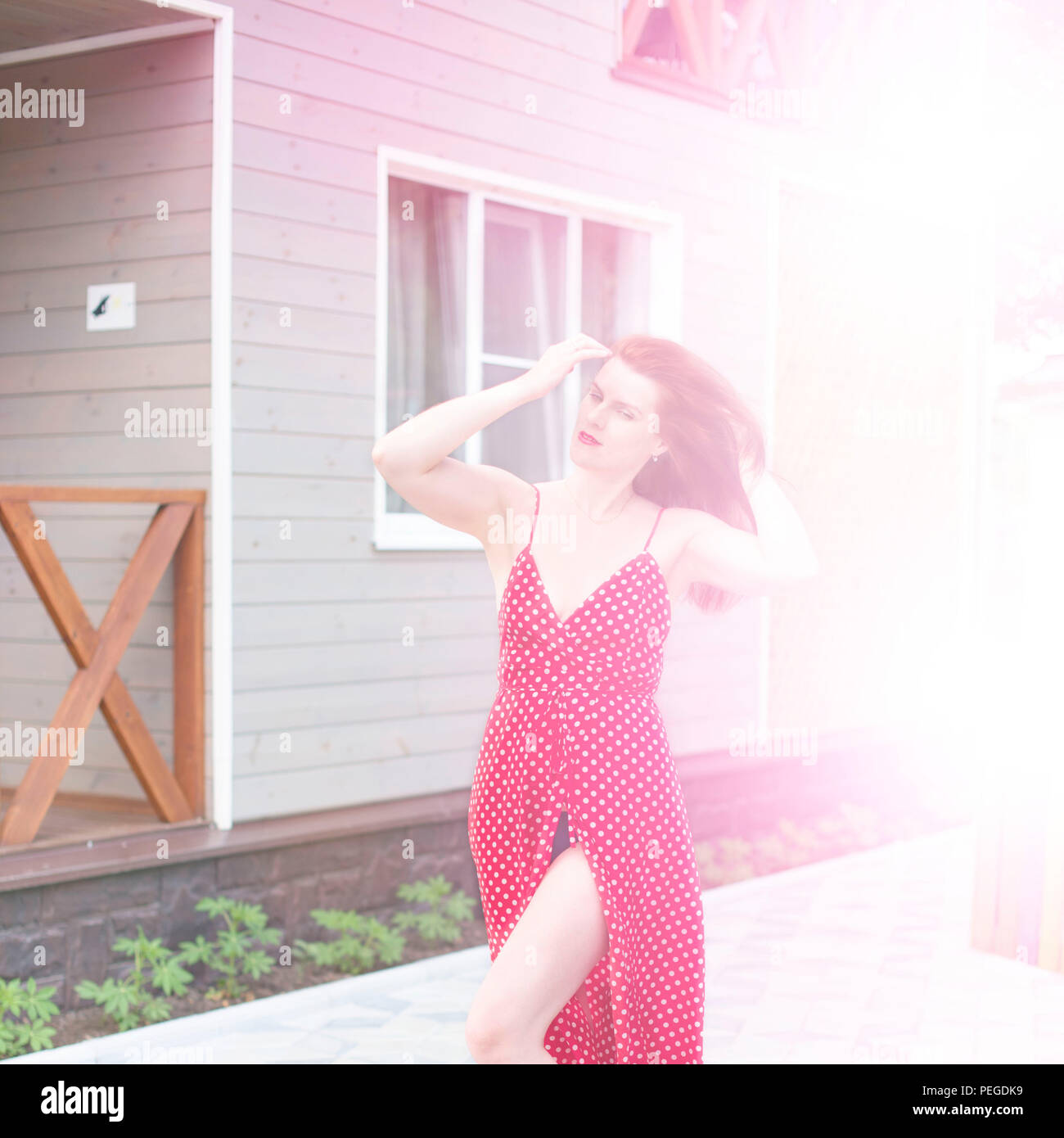 Defocalizzazione giovane donna a piedi in strada gioia sorridenti. Bruna in abito rosso sole lifestyle Foto Stock