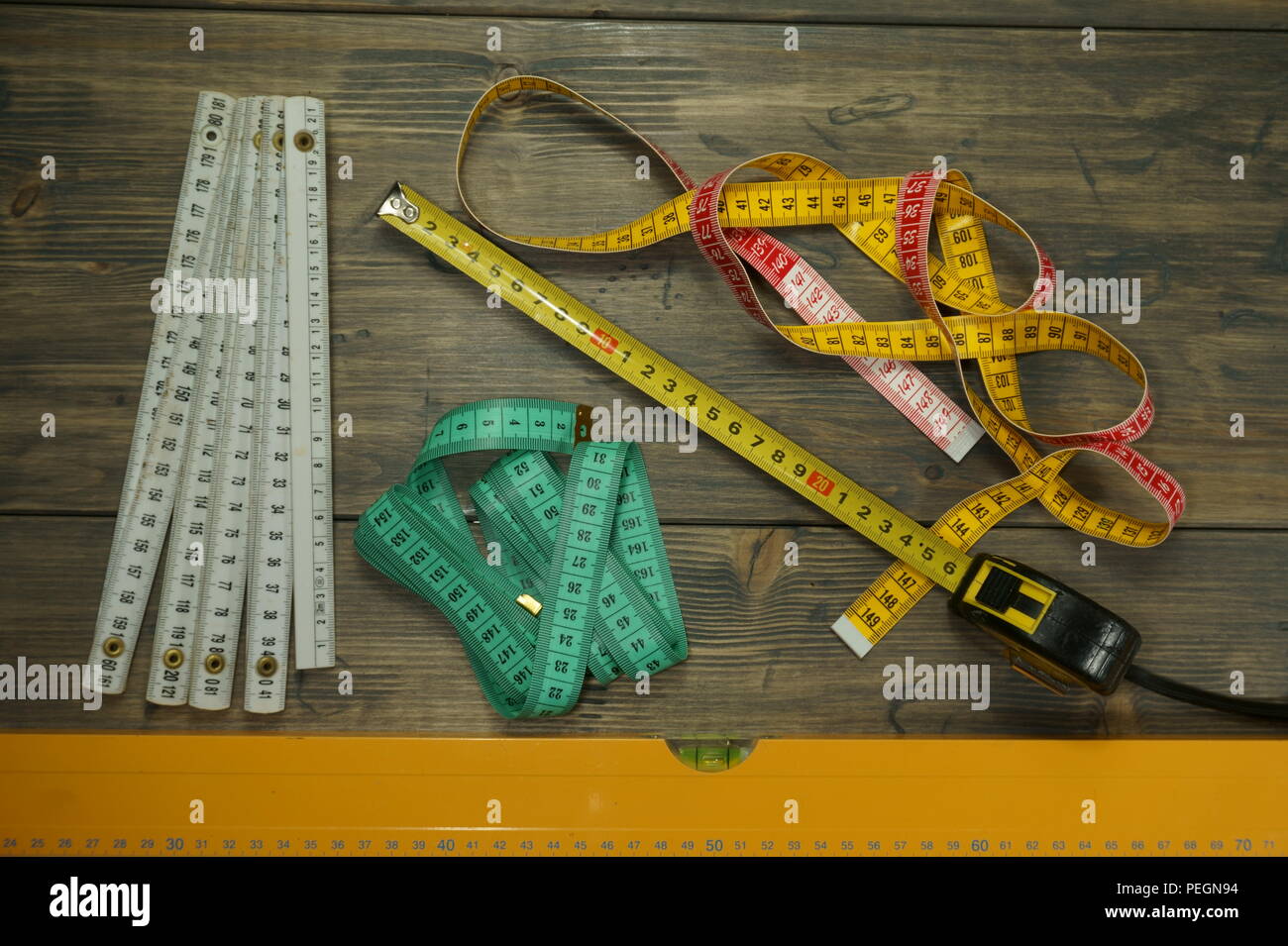 Selezione di differenti strumenti di misurazione su un rustico sfondo di legno con una scala graduata di livello di spirito e un assortimento di misure lineari a nastro Foto Stock