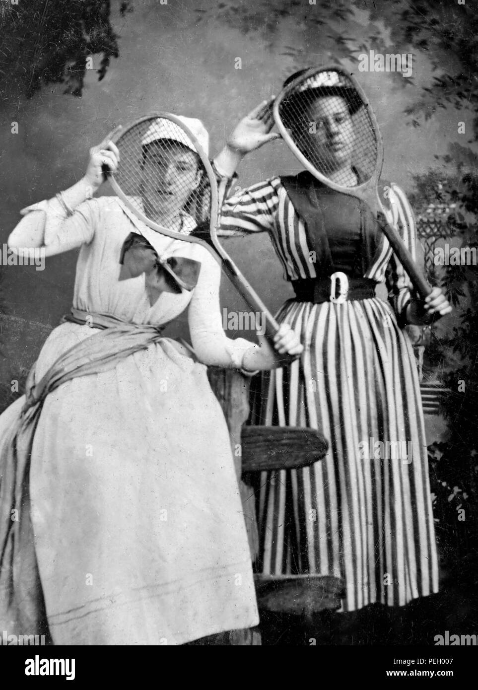 Due donne in abiti sportivi scherzosamente posano con loro racchette da tennis in un palazzo di fine ottocento tintype immagine, ca. 1890. Foto Stock