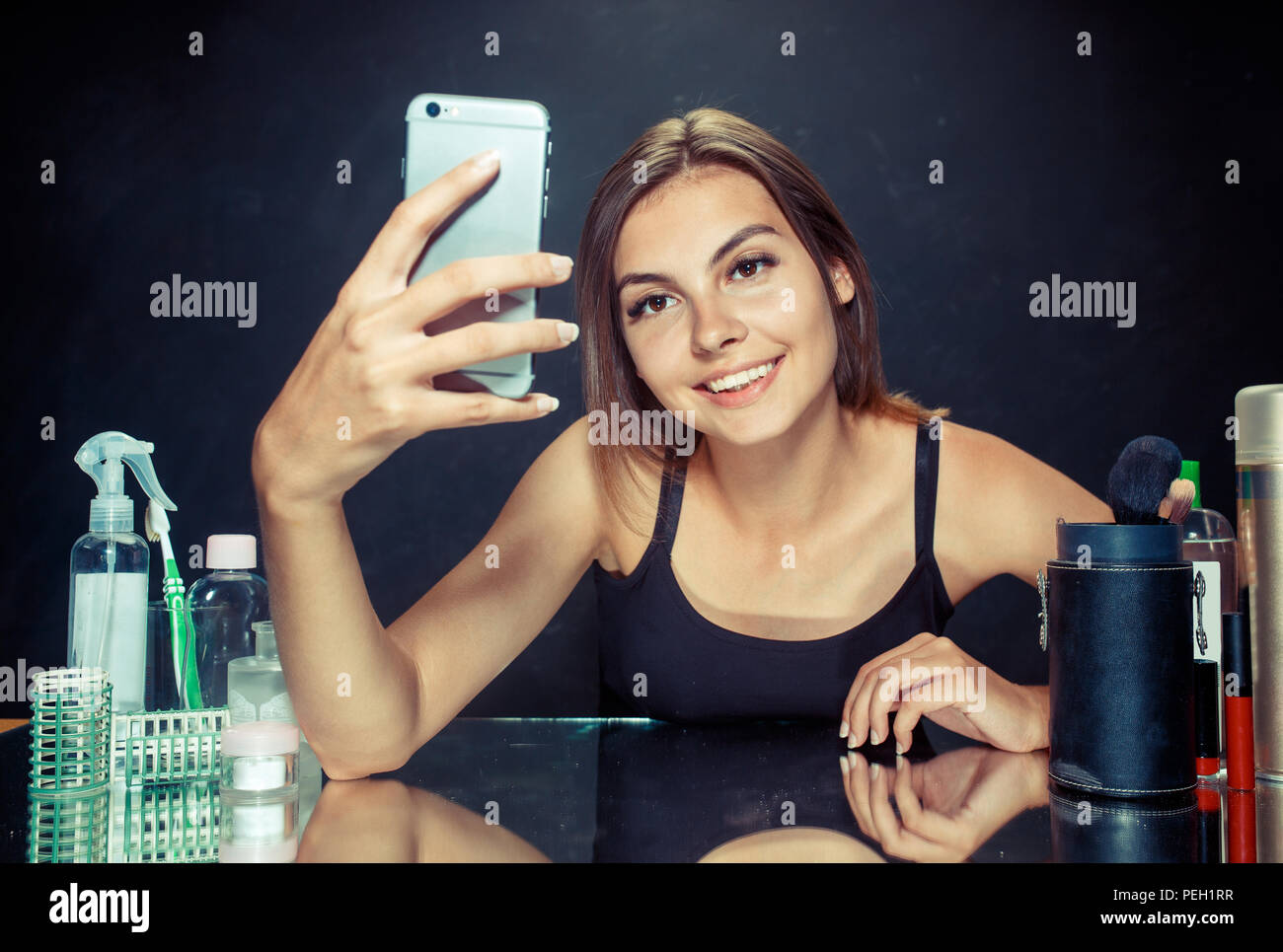 La bellezza della donna dopo aver applicato il trucco.La bellezza della donna con il trucco. Bella ragazza guardando il telefono mobile e rendendo selfie foto . Mattina, il make up e le emozioni umane concetto. Modello caucasico allo studio Foto Stock