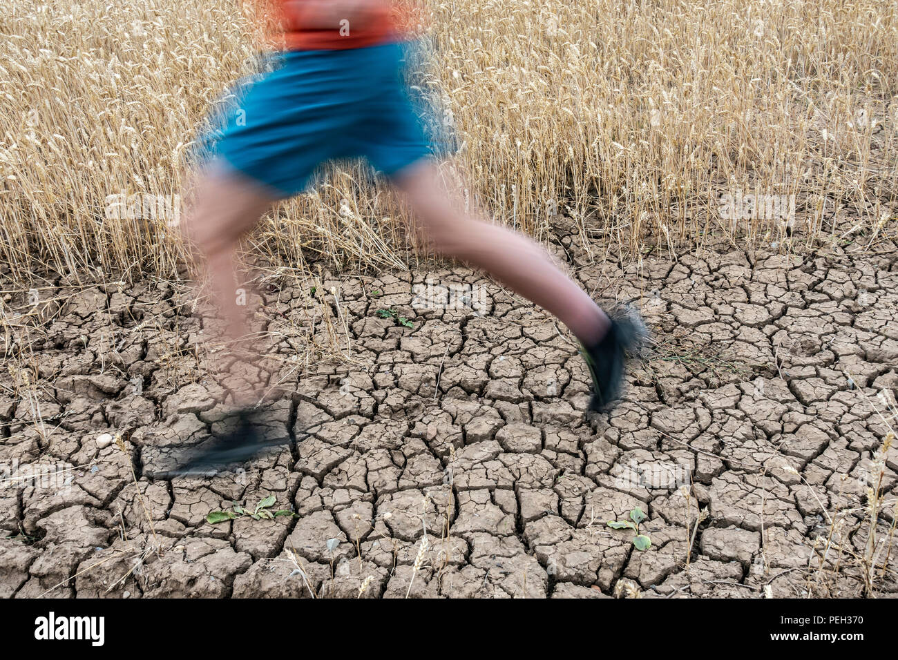 Uomo che corre su terra rotto durante la siccità. Regno Unito. Il cambiamento climatico e il riscaldamento globale del concetto. Foto Stock