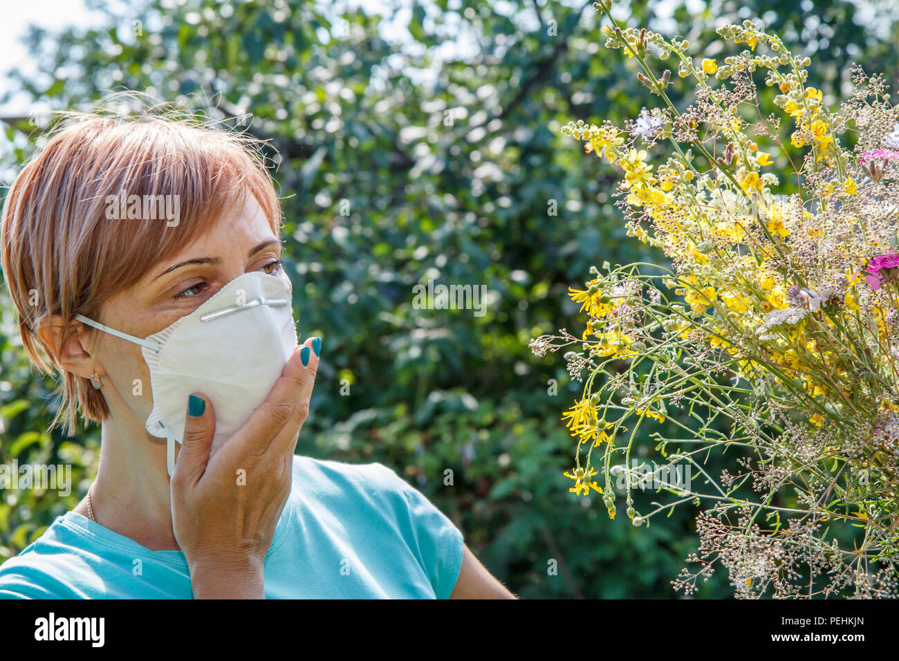 Donna in maschera protettiva holding bouquet di fiori selvaggi e nel tentativo di combattere le allergie al polline. Donna proteggendo il suo naso da allergeni Foto Stock