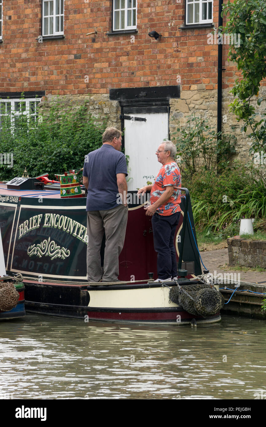 Due uomini di mezza età avente una chat su un narrowboat denominato breve incontro; Grand Union Canal, Stoke Bruerne, Northamptonshire, Regno Unito Foto Stock