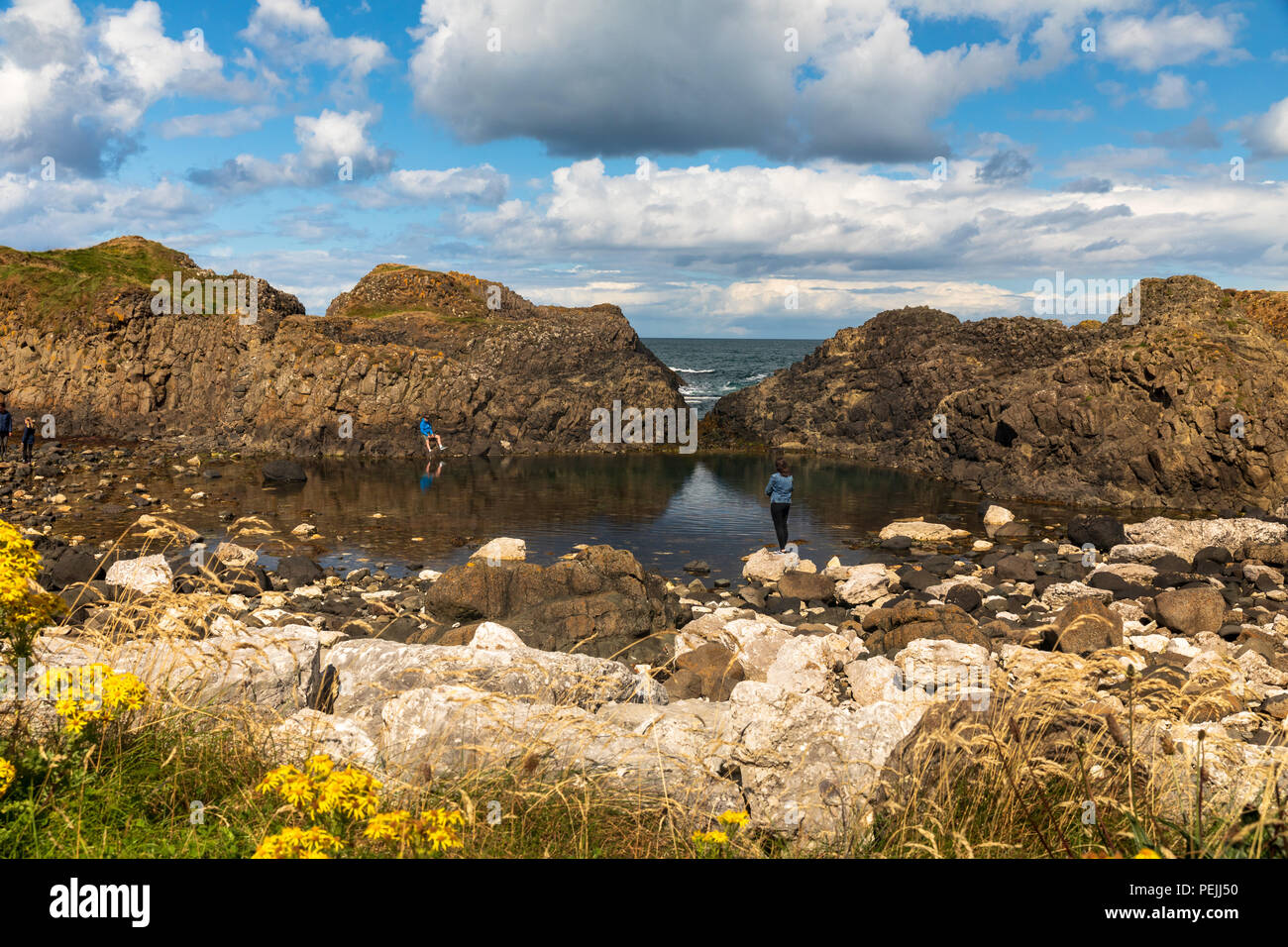 Vista panoramica di Ballintoy, Co Antrim, Irlanda del Nord in estate con due persone in un momento di relax a bordo dell'acqua Foto Stock