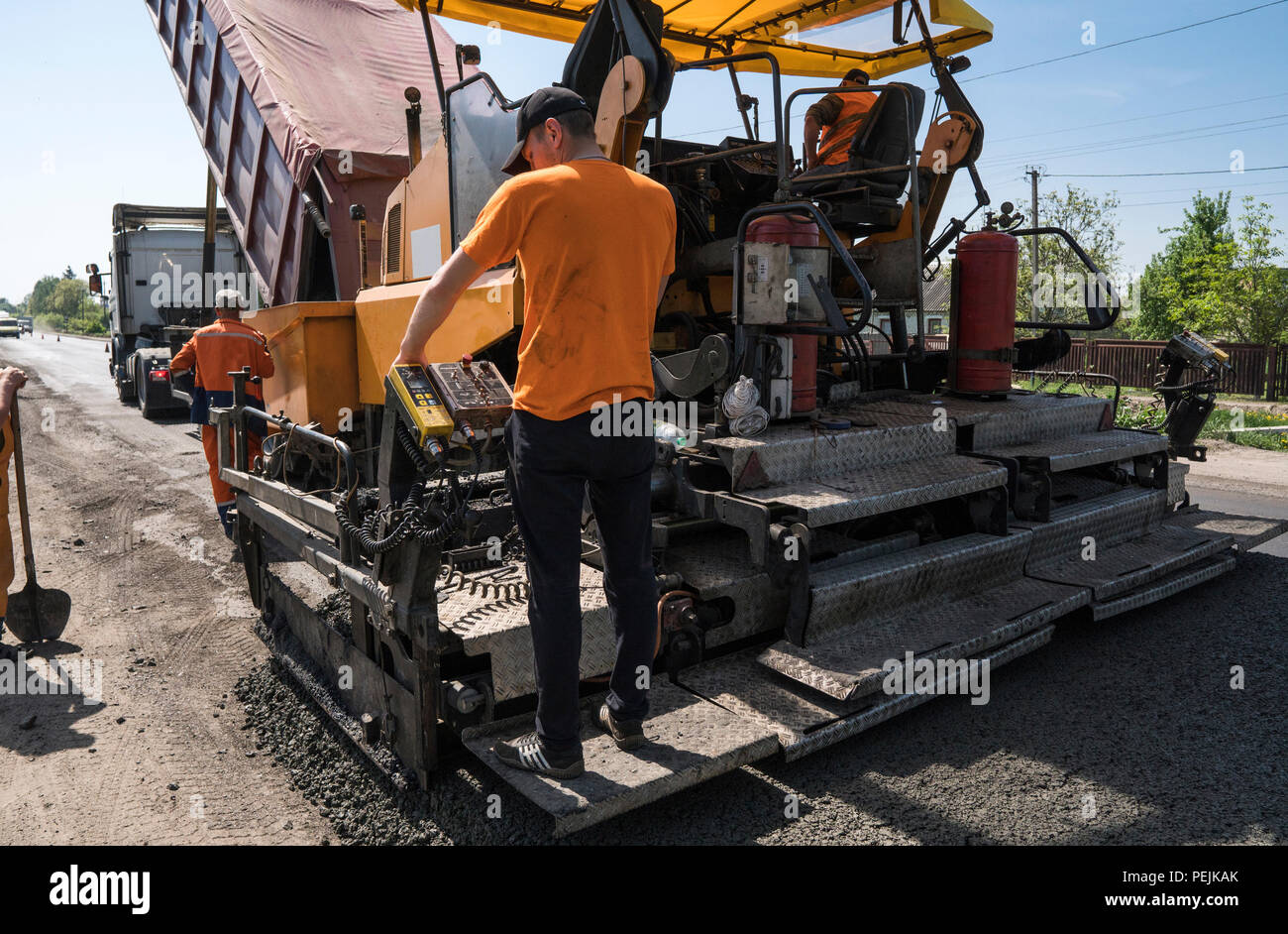 Lavoratore di asfalto operativo lastricatore macchina durante la costruzione di strade e lavori di riparazione. Un lastricatore finisher, asfalto di finitura o macchina di pavimentazione disporre uno strato di asfalto. Ripavimentazione. Foto Stock